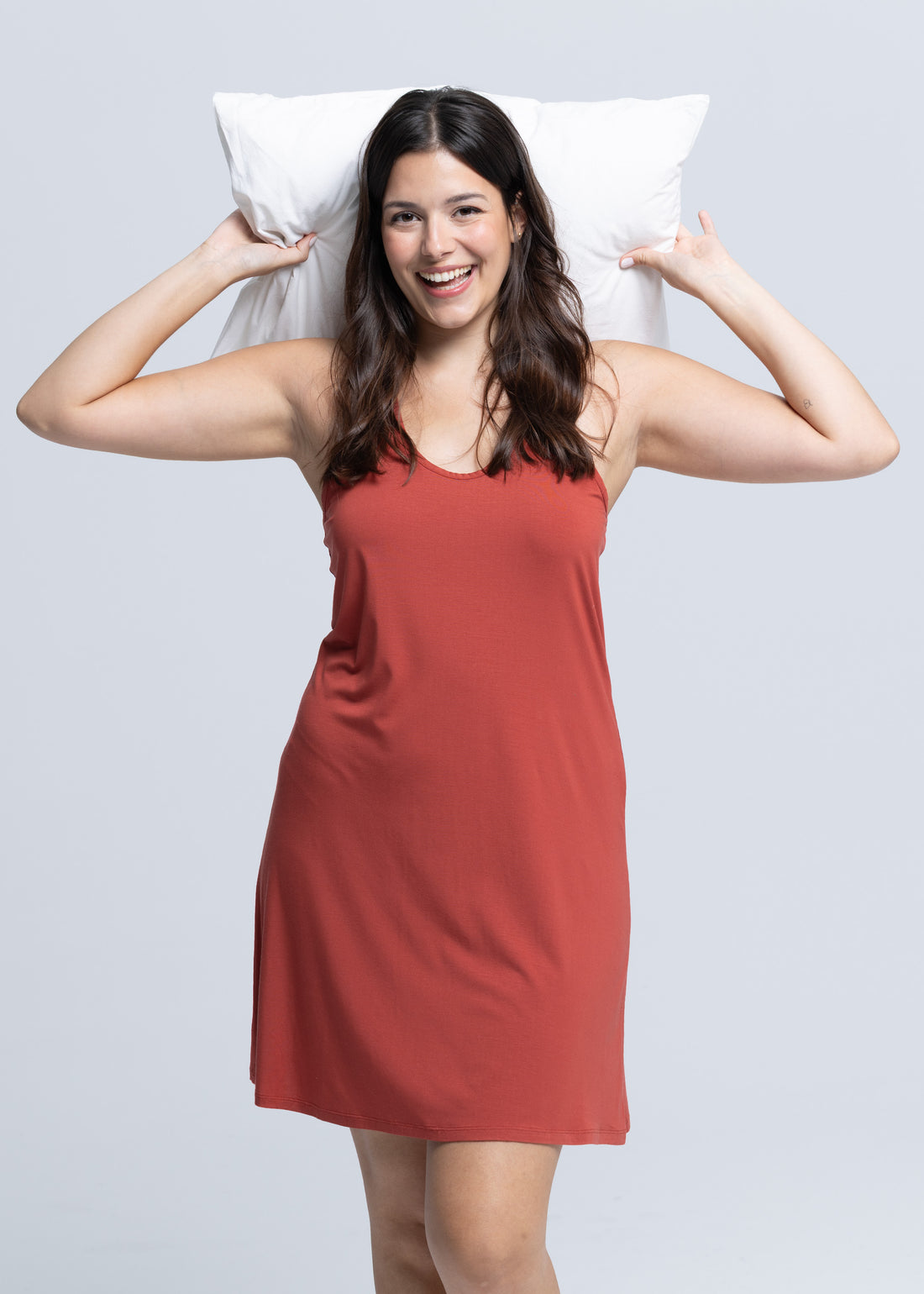 Woman wearing new Golden Hour collection dress and holding a pillow near her head ready for bed.