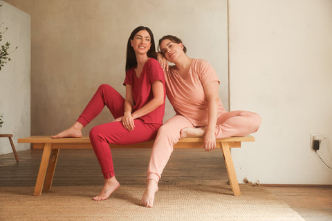 Two women sitting on a wooden bench in a room with a neutral color scheme.